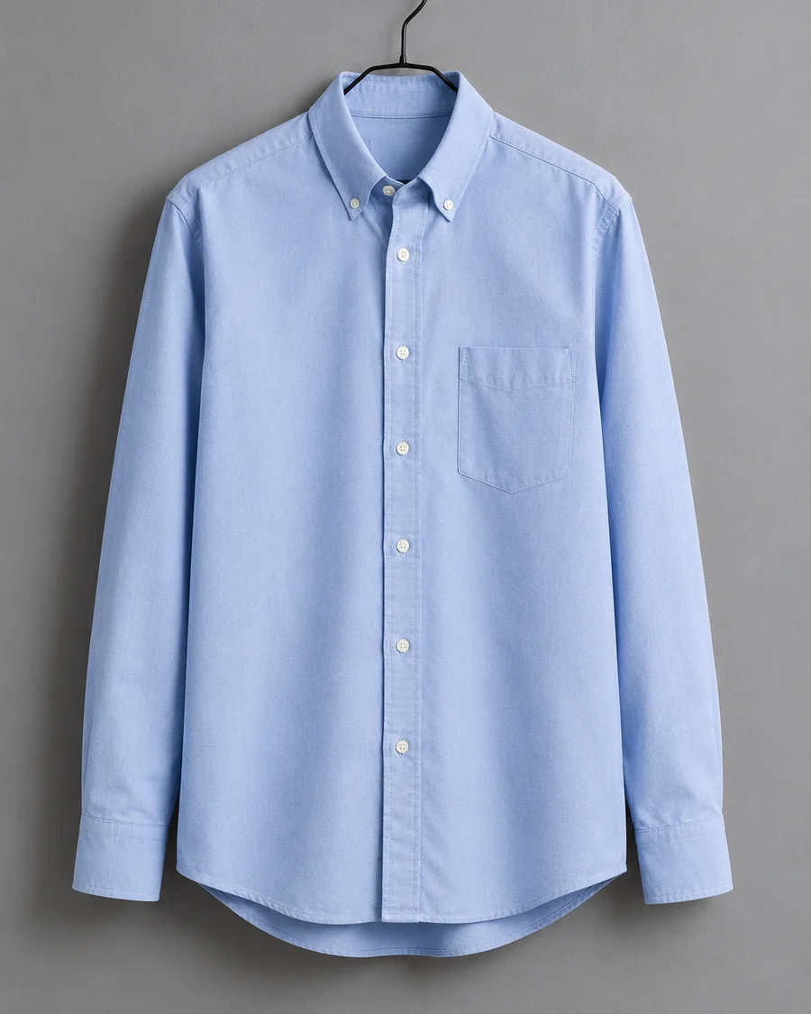 Camisa oxford azul claro de cuello abotonado colgada en una percha negra de metal
